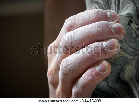 Chalked hand grips tightly to hang off an artificial climbing hold. Shallow depth of field