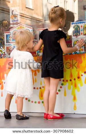 two little girls looking at a shop window and select goods