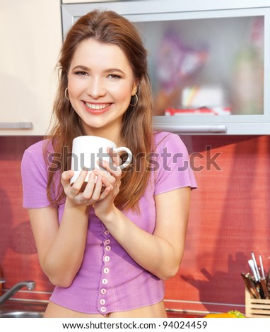 Attractive young woman with cup of tea smiling and joyful looking to the camera in the modern kitchen