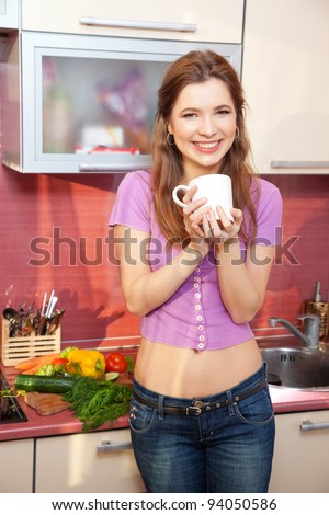 Attractive young woman with cup of tea smiling and joyful looking to the camera in the modern kitchen