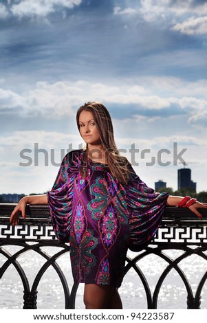 Attractive young woman in violet dress looking to the camera near the river in sunny day