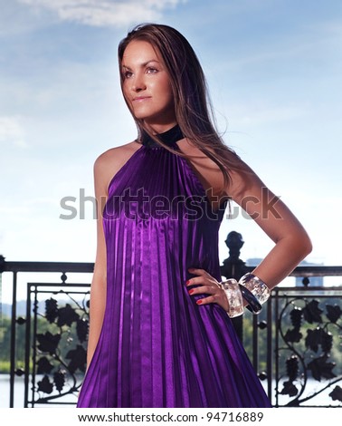 Attractive young woman in violet dress looking out of the camera near the river in sunny day
