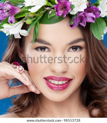 Attractive young woman with diamonds on the hand and flowers on the head looking to the camera on the blue background