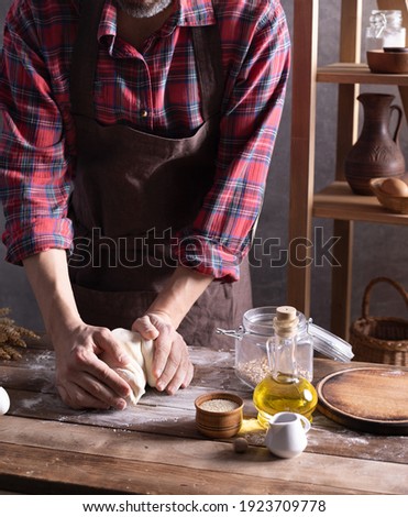 Baker man kneading or making dough and bakery ingredients for homemade bread cooking on table. Bakery concept near wall background texture