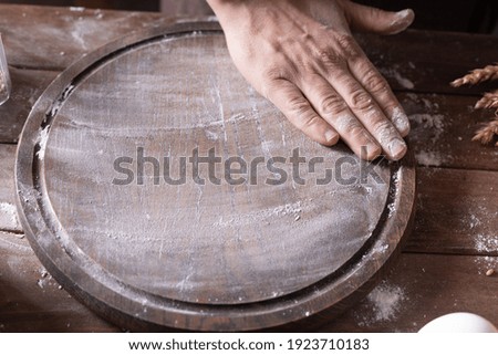 Baker male hand scattering flour for kneading dough and bakery ingredients with homemade bread cooking on wooden pizza board. Bakery concept with and wooden tabletop background texture