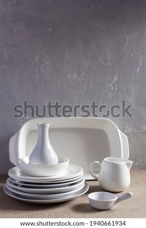 Empty crockery or ceramic dishes set. White kitchen dishware and tableware wooden table near grey wall background texture