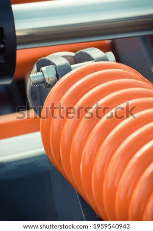 Big and hard orange steel spring as part and detail of industrial or agricultural machine. Technology