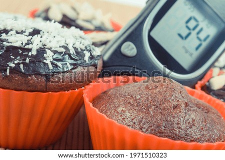 Glucometer with result of measurement sugar level and fresh baked chocolate muffins. Diabetes and dessert for different occasions
