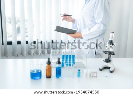 Scientist woman standing to reading result coronavirus vaccine on report after using microscope and test tube with blue liquid to experiment produce vaccine covid-19 in laboratory