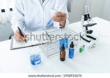 Scientist woman holding test tube in her hands and writing down result report on notebook while working to analyzing and developing coronavirus vaccine in laboratory