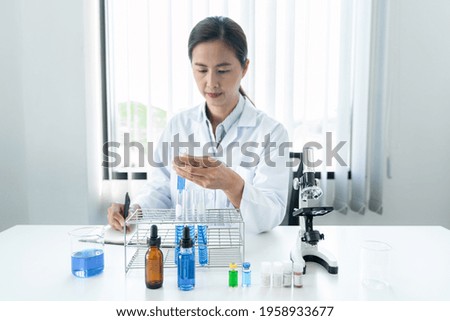 Scientist woman holding test tube in her hands and writing down result report on notebook while working to analyzing and developing coronavirus vaccine in laboratory