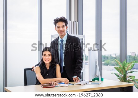 Asian businessman and businesswoman discussing with computer at desk, working together at workplace office, looking at camera.