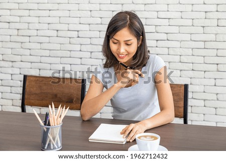 Young attractive Asian woman smiling thinking planning writing memo in notebook working from home