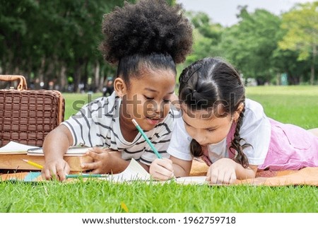 Two american african little girl lying and drawing with colored pencils at summer park, feel happiness, outdoor education concepts