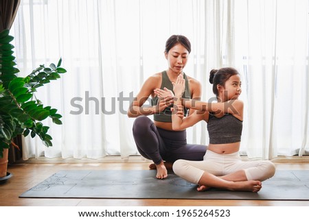 Asian young mother teaching her daughter to yoga pose and exercise together on yoga mat in living room at home. New normal lifestyle concept. Healthy lifestyle. Relaxing at home