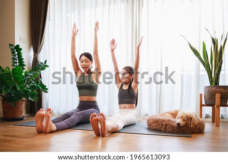 Asian young mother teaching her daughter to yoga pose and exercise together with their dog on yoga mat in living room at home. New normal lifestyle concept. Healthy lifestyle. Relaxing at home