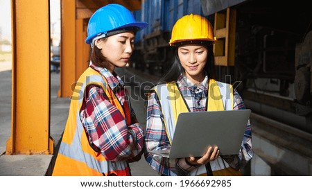 Successful Rail logistics specialists or train engineers wearing helmets and safety vests are conducting inspections and meeting a work plan for repairing a freight train in the factory.
