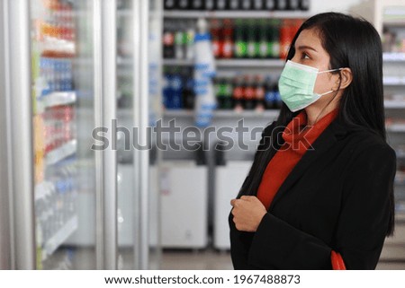 Young smart business asian woman wearing face mask looking and choosing grocery to buy from shelf in supermarket department store or shopping mall, new normal coronavirus crisis or covid19 outbreak.