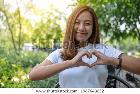 A beautiful asian woman making heart hand sign in the outdoors
