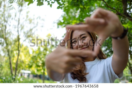 Portrait image of a beautiful asian woman raising hands and playing with camera in park