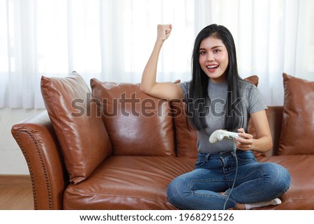 VDO game console station concept. active asian woman sitting on sofa, holding joystick and playing exciting game. Cute girl looked excited with game controller console