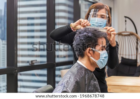 Young man getting haircut by hairdresser in living room, Barber using scissors and comb, New normal concepts
