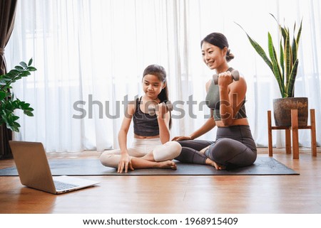 Mom and Little Girl doing dumbbell exercises by using online learning with a laptop computer on a yoga mat in the living room at home. New normal concept. Healthy lifestyle. Relaxing at home