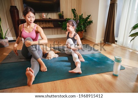 Mom and Little Girl doing exercises by using online learning with a laptop computer on a yoga mat in the living room at home. New normal concept. Healthy lifestyle. Relaxing at home