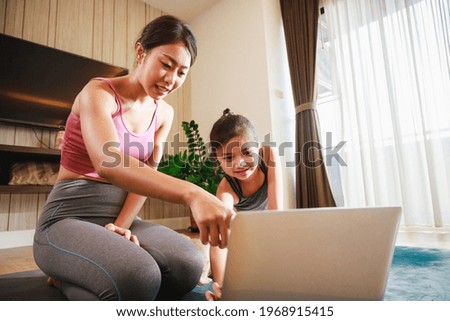 Asian woman and daughter practicing yoga from yoga online course via laptop at home. Healthy lifestyle - technology at home. New normal lifestyle. Home Online Stretching Yoga Fitness Exercise.