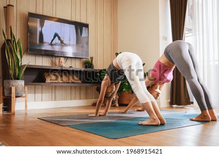Asian woman and Little girl practicing yoga from yoga online course via smart TV at home. Healthy lifestyle - technology at home. New normal lifestyle. Home Online Stretching Yoga Fitness Exercise.