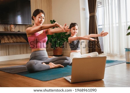 Asian woman and Little girl practicing yoga from yoga online course via laptop at home. Healthy lifestyle - technology at home. New normal lifestyle. Home Online Stretching Yoga Fitness Exercise.