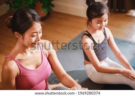 Mom and Little Girl doing exercises by using online learning with a laptop computer on a yoga mat in the living room at home. New normal concept. Healthy lifestyle. Relaxing at home