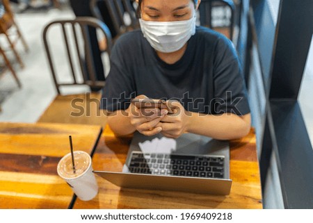Woman wearing disposable mask while using smartphone in coffee shop