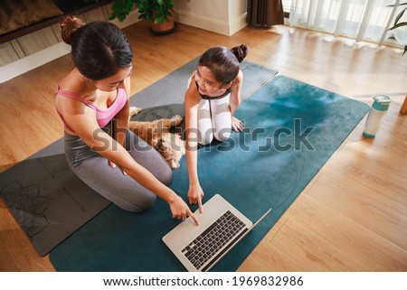 Asian woman and daughter practicing yoga from yoga online course via laptop at home. Healthy lifestyle - technology at home. New normal lifestyle. Home Online Stretching Yoga Fitness Exercise.