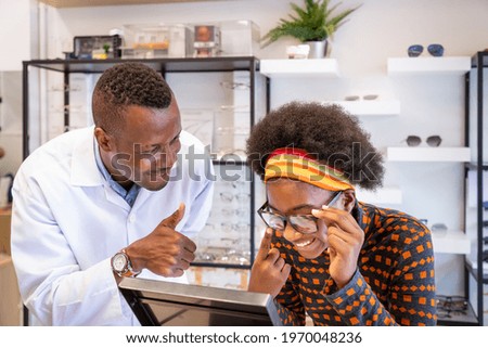 African optician explaining and selling eyeglasses to young woman girl customer in optical shop store. Eyecare concept.
