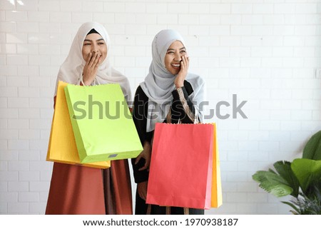 two young muslim shopper women standing and holding shopping bags in shopping mall with happy smiling face