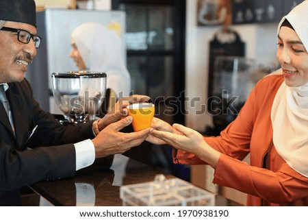 muslim customer businessman wearing black suit receive a cup of coffee from young muslim barista girls at coffee shop counter