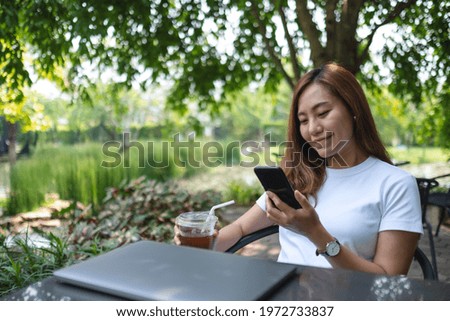 A beautiful young asian woman using mobile phone with laptop computer on the table in the park