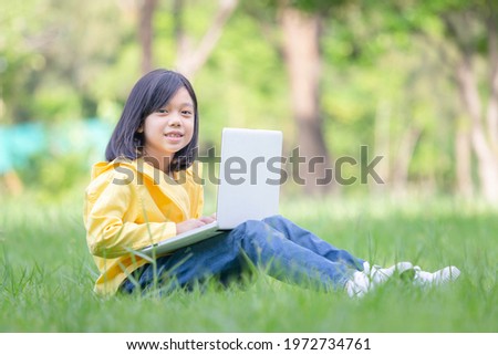 Asian  kid girl sitting on the grass studying with laptop in the park, Outdoor learning concepts