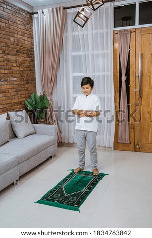 boy prays to God with his arms united on the prayer mat