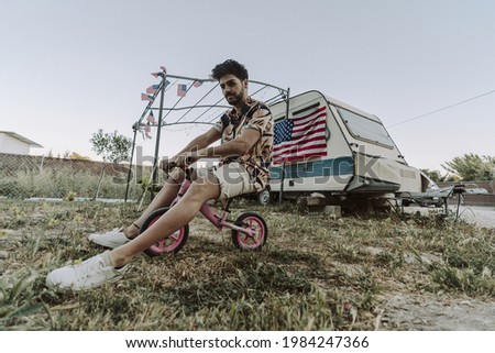 A young Spanish male sitting on a small pink bike and having fun on background of the US flag