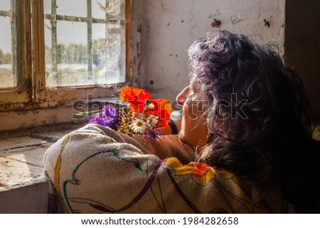 A senior blue-haired female sitting near the window with beautiful flowers