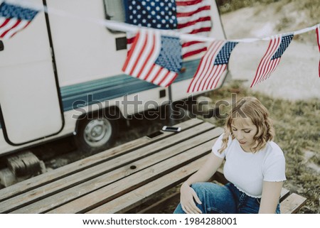 A beautiful Spanish female sitting on picnic chair seen through US flags - US Independence day