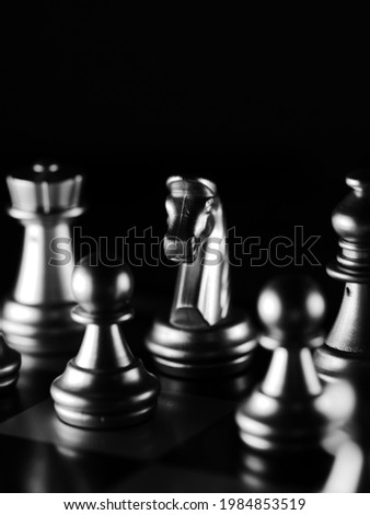 A dramatic grayscale shot of chess figures lit in the darkness