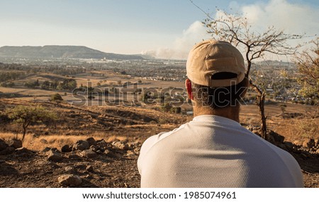 A  rear view of a man on top of a hill enjoying the beautiful landscape