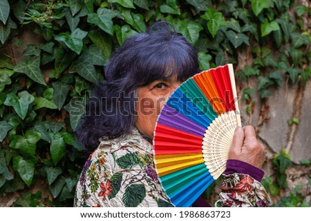 A Hispanic senior female posing with a hand fan with the LGBT flag colors