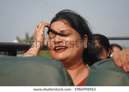 An Indian woman in an open bus smiling and touching her hair with closed eyes during a windy weather