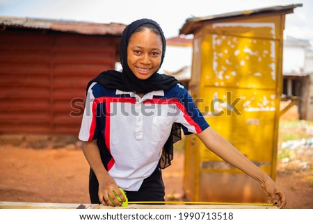 A professional female African carpenter smiling as she takes a measurement of wood