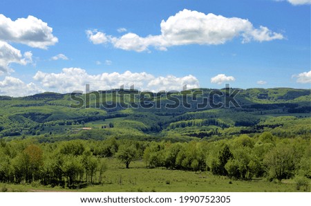 A sunny day with bright white clouds above vast green hills and trees