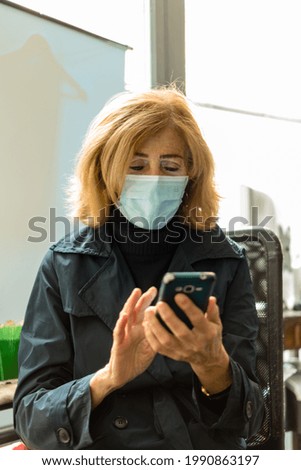 A vertical shot of a middle-aged Italian woman, wearing a face mask and using her smartphone